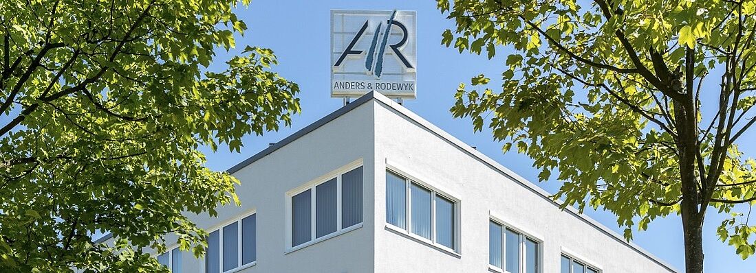 Referenz AR Gebäude Gebäudeecke zwischen Bäumen mit dem Logo von Anders und Rodewyk