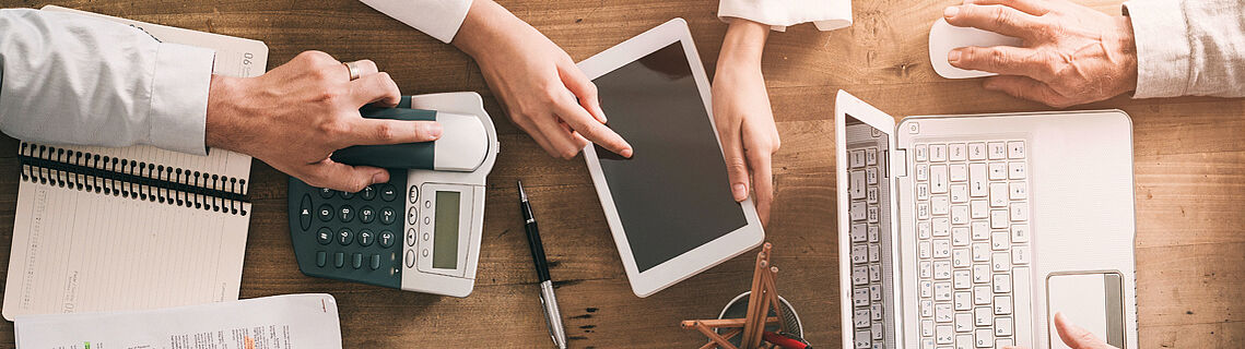 3 Personen an einem Schreibtisch mit Laptop und Smartphone