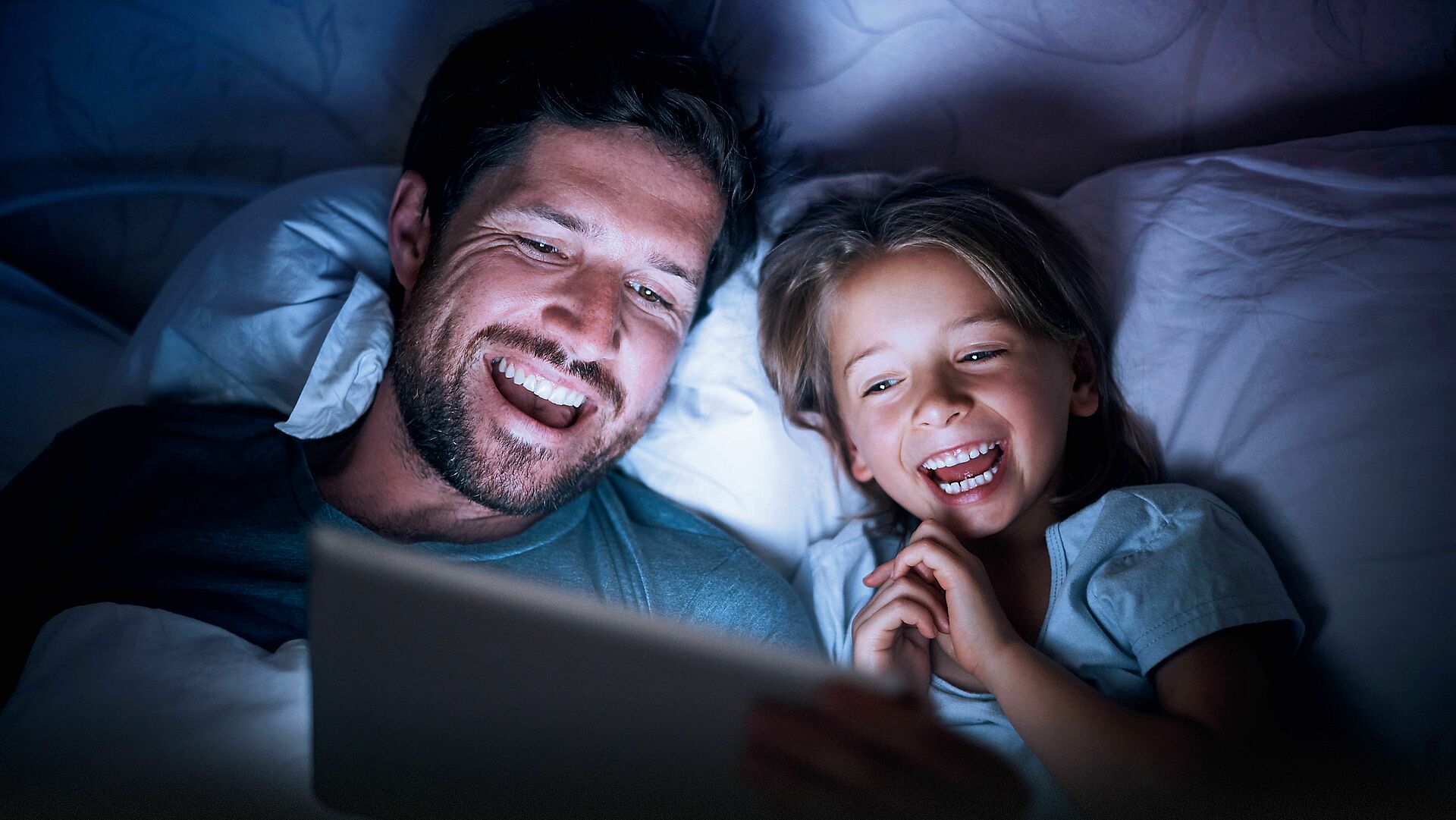 Vater und Sohn liegen im Bett und gucken auf einem Laptop über waipu tv fernsehen